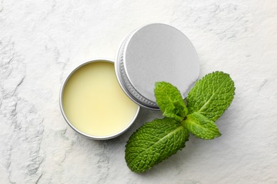 Photo of Mint lip balm and green leaves on beige textured background, top view. Cosmetic product