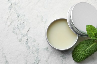 Photo of Mint lip balm and green leaves on beige textured background, top view. Space for text