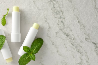 Photo of Mint lip balms and green leaves on beige textured background, flat lay. Space for text