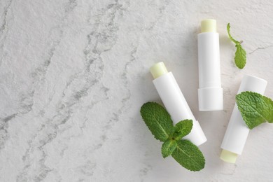 Photo of Mint lip balms and green leaves on beige textured background, flat lay. Space for text