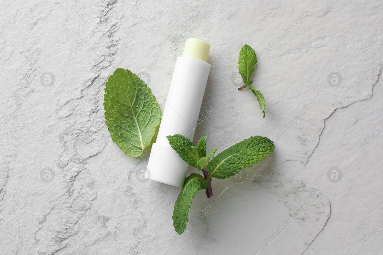 Photo of Mint lip balm and green leaves on beige textured table, flat lay. Cosmetic product