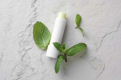 Photo of Mint lip balm and green leaves on beige textured table, flat lay. Cosmetic product