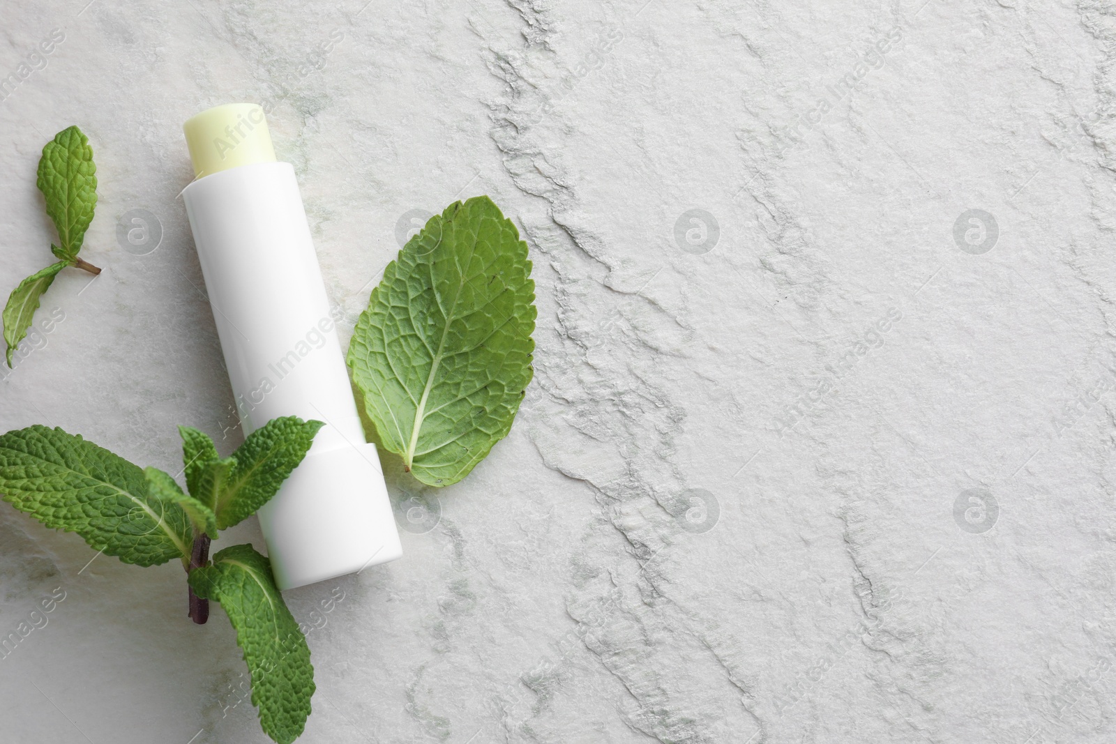 Photo of Mint lip balm and green leaves on beige textured background, flat lay. Space for text