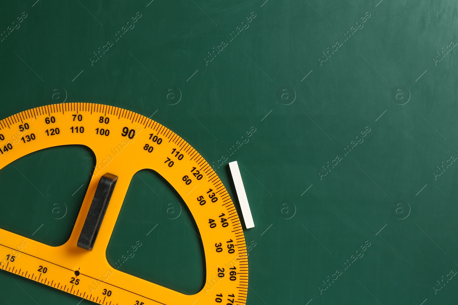 Photo of Protractor ruler and chalk on green chalkboard, top view. Space for text