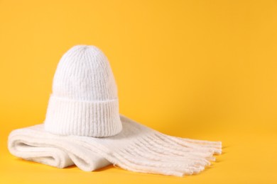 Photo of Stylish knitted hat and warm scarf on yellow background, space for text