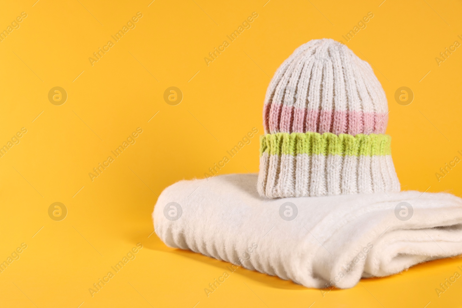 Photo of Stylish knitted hat and warm scarf on yellow background, space for text