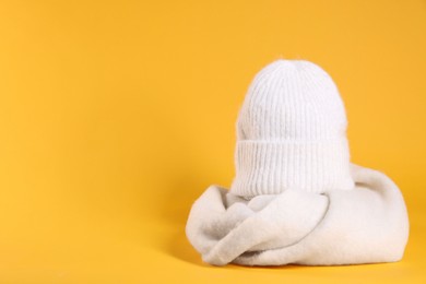 Photo of Stylish knitted hat and warm scarf on yellow background, space for text