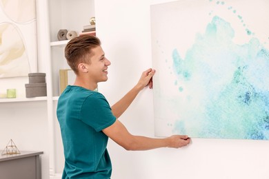 Photo of Smiling young decorator hanging abstract picture indoors