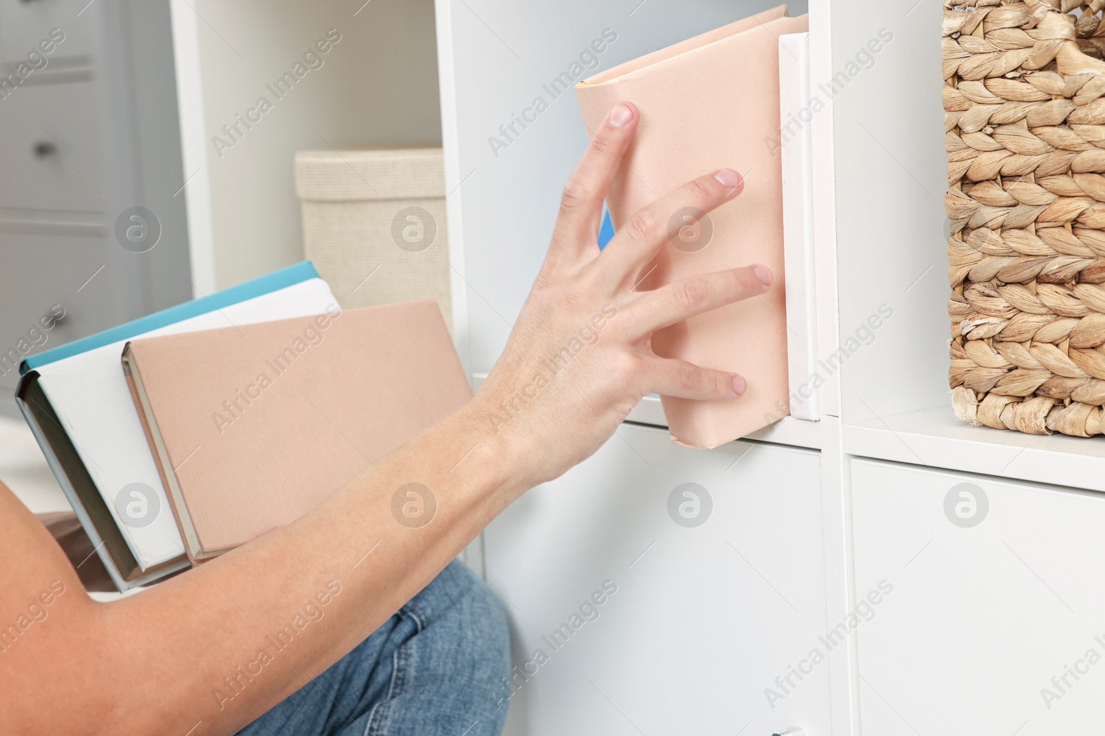 Photo of Male decorator arranging books onto shelf indoors, closeup