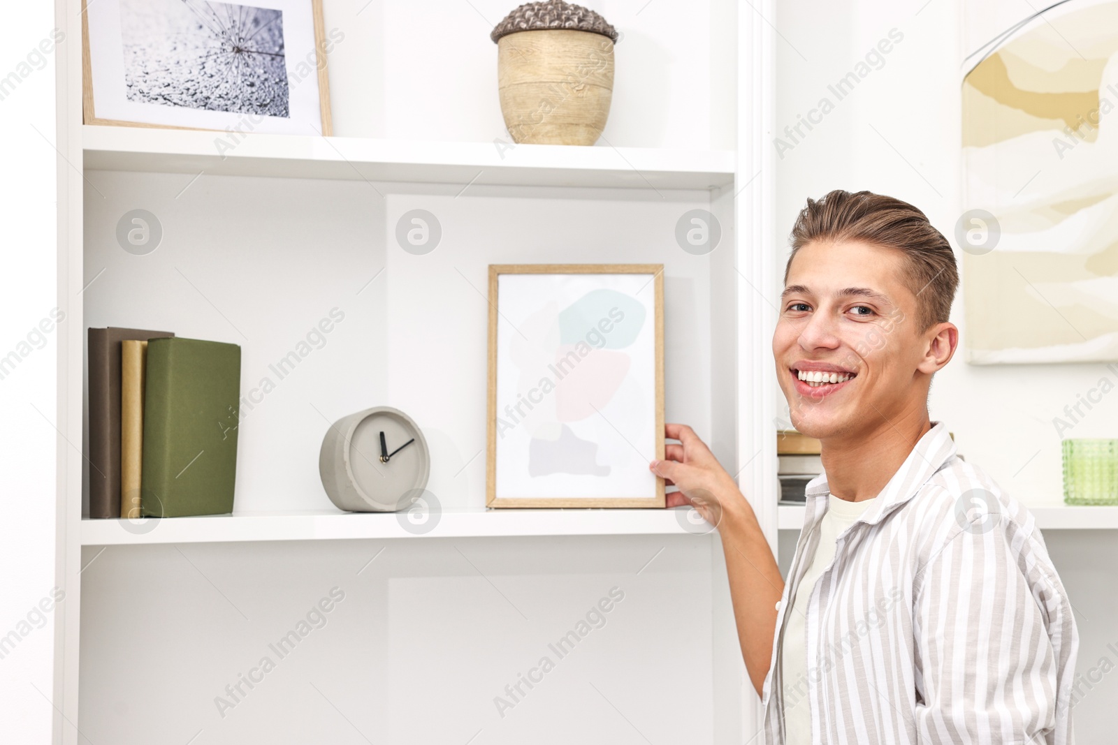 Photo of Smiling decorator with abstract picture near shelving unit indoors