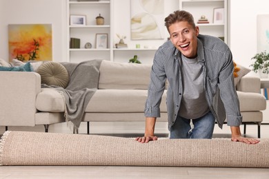 Photo of Happy decorator rolling out beige carpet indoors