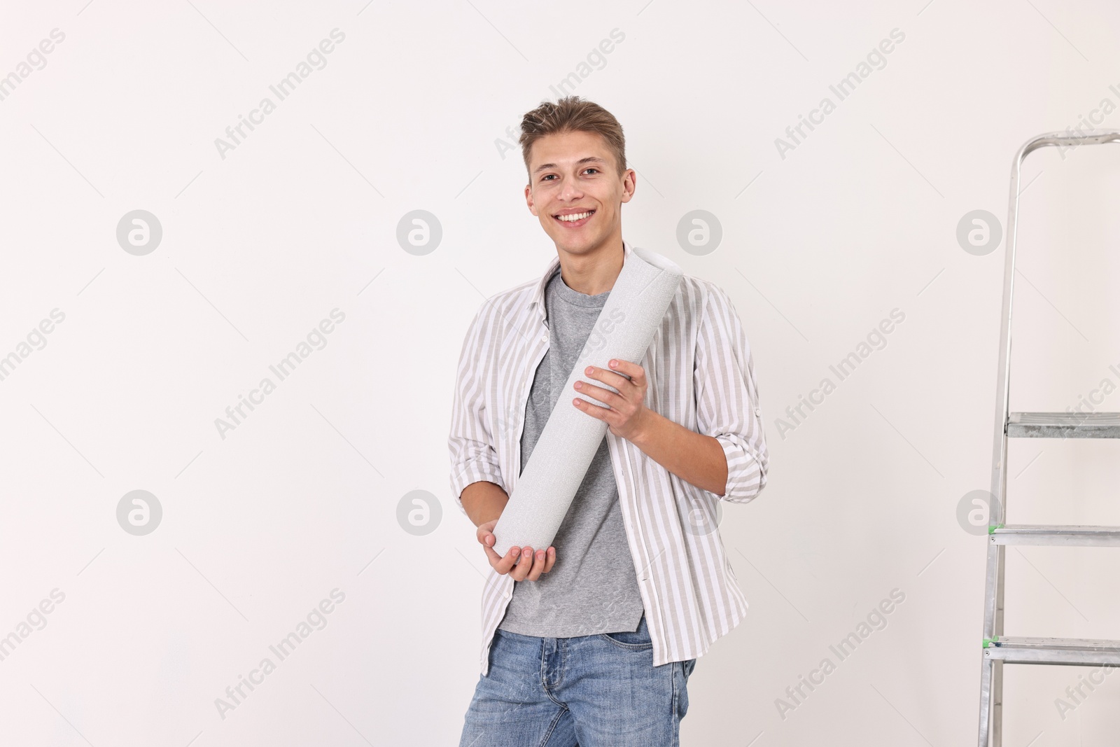 Photo of Smiling handyman with roll of wallpaper indoors