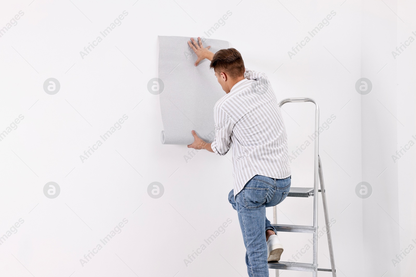 Photo of Male handyman hanging gray wallpaper indoors, back view. Space for text