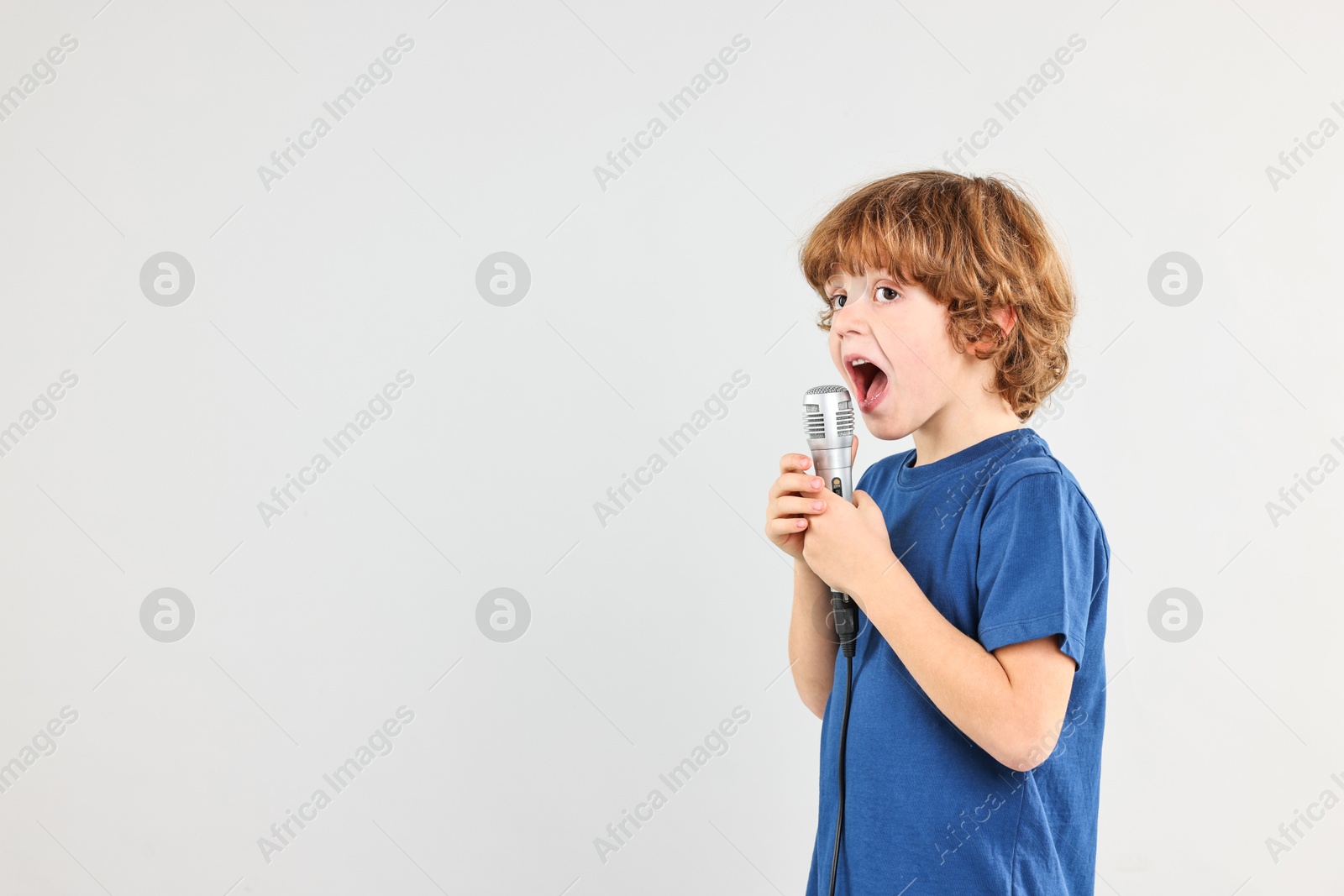 Photo of Little boy with microphone singing on light grey background, space for text