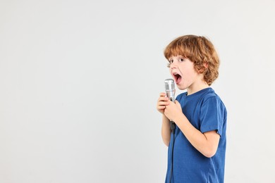 Photo of Little boy with microphone singing on light grey background, space for text