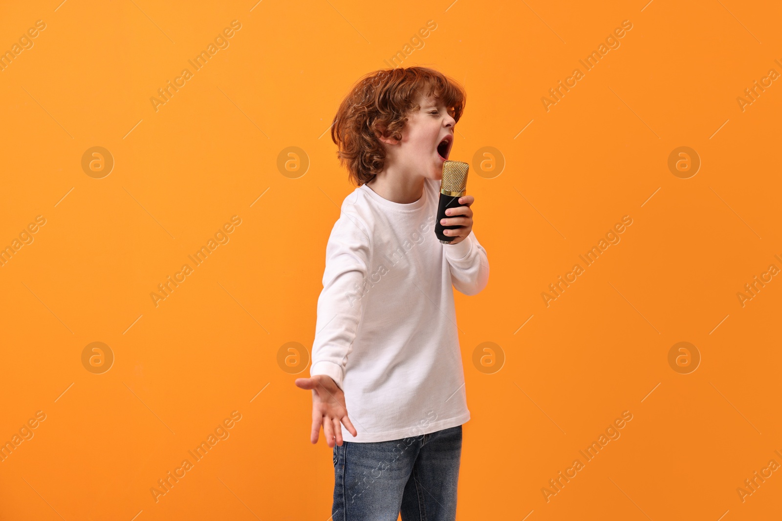 Photo of Little boy with microphone singing on orange background