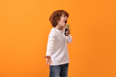 Photo of Little boy with microphone singing on orange background