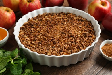 Photo of Tasty apple crisp in baking dish and ingredients on wooden table, closeup