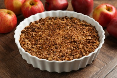 Photo of Tasty apple crisp in baking dish and fresh fruits on wooden table, closeup