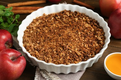 Photo of Tasty apple crisp in baking dish and ingredients on wooden table, closeup