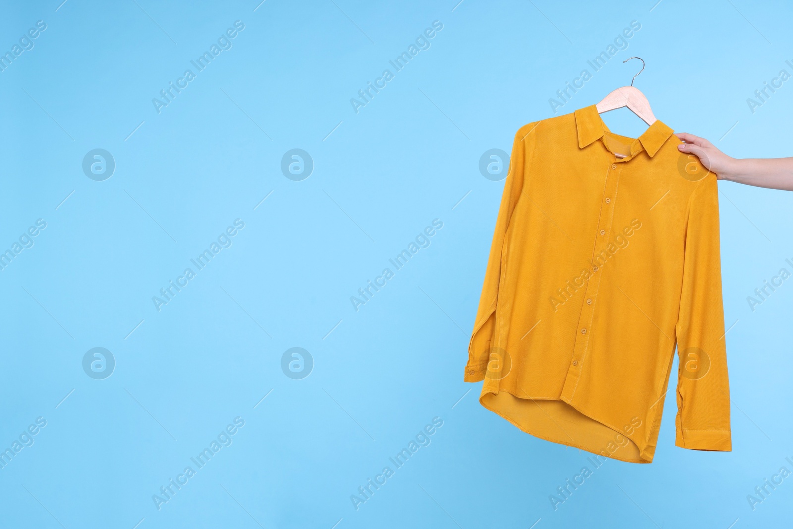 Photo of Woman holding hanger with orange shirt on light blue background, closeup. Space for text