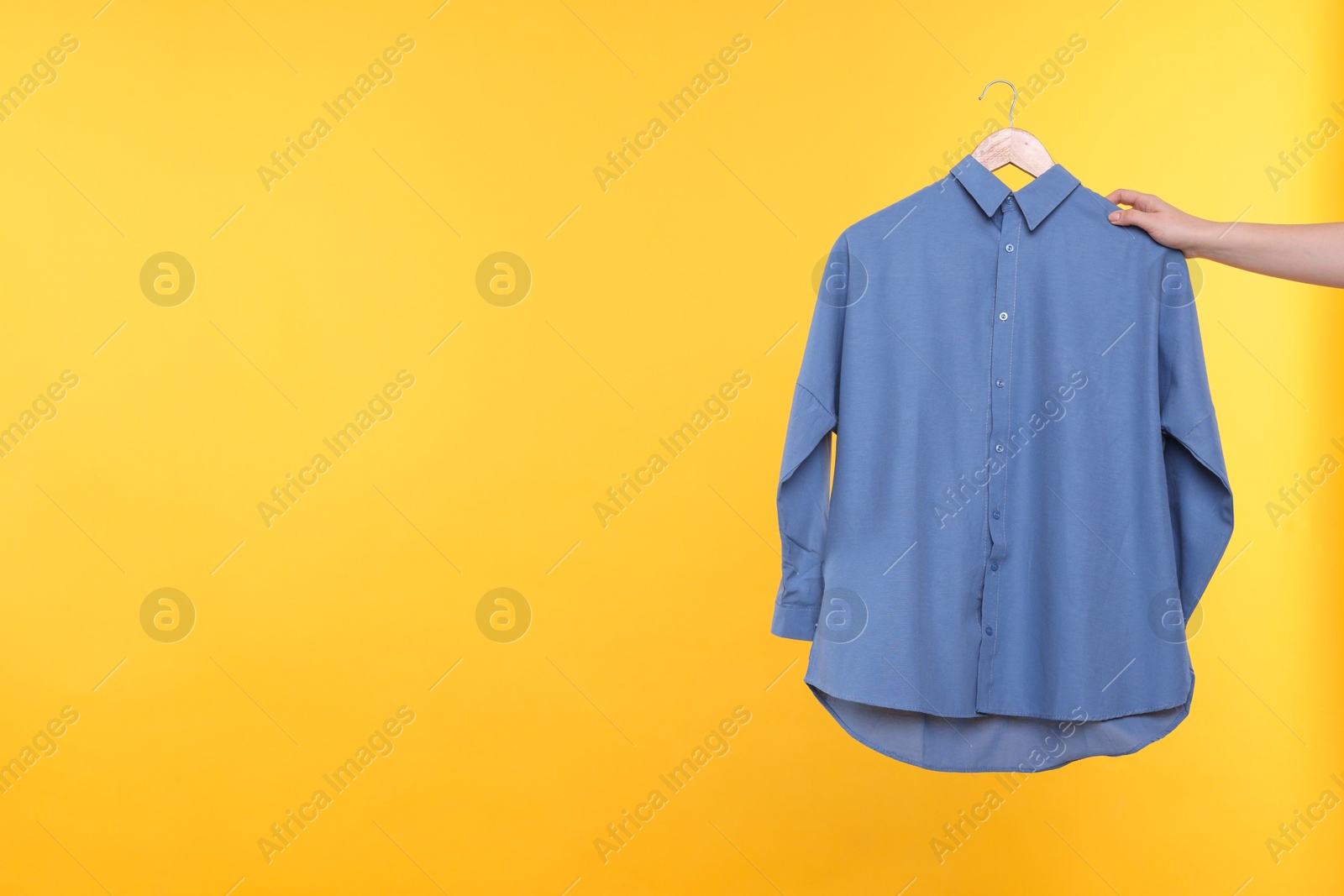 Photo of Woman holding hanger with blue shirt on yellow background, closeup. Space for text