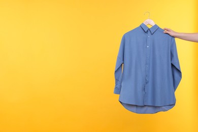 Photo of Woman holding hanger with blue shirt on yellow background, closeup. Space for text