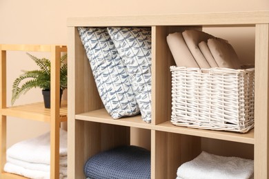 Photo of Home textile organization. Different pillows, linens and blankets on shelving units near beige wall