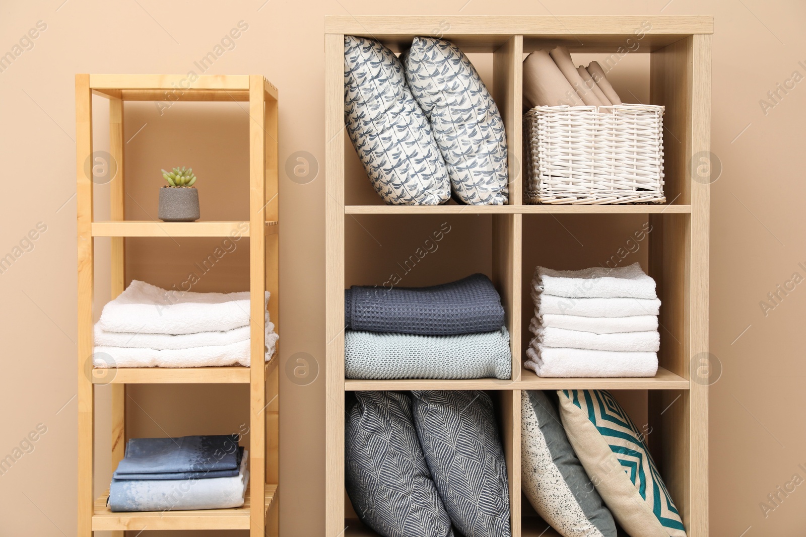 Photo of Home textile organization. Different pillows, linens towels and blankets on shelving units near beige wall