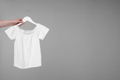 Photo of Woman holding hanger with sweater vest on light grey background, closeup. Space for text