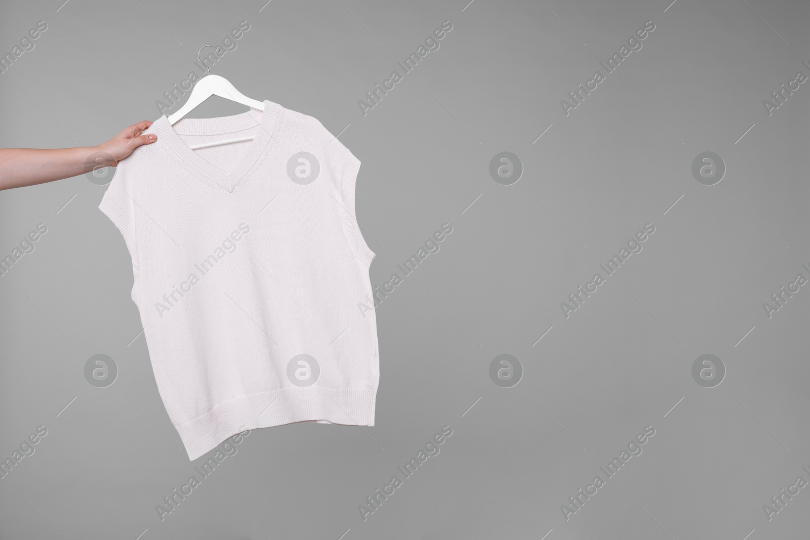 Photo of Woman holding hanger with sweater vest on light grey background, closeup. Space for text