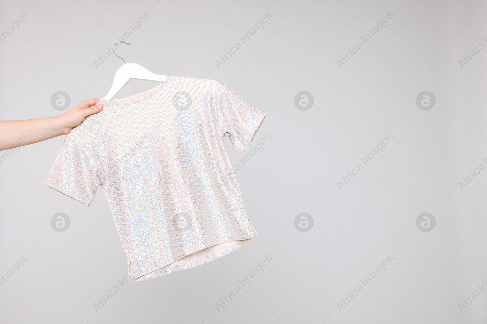 Photo of Woman holding hanger with stylish t-shirt on light grey background, closeup. Space for text