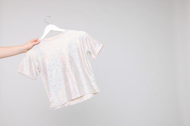 Photo of Woman holding hanger with stylish t-shirt on light grey background, closeup. Space for text