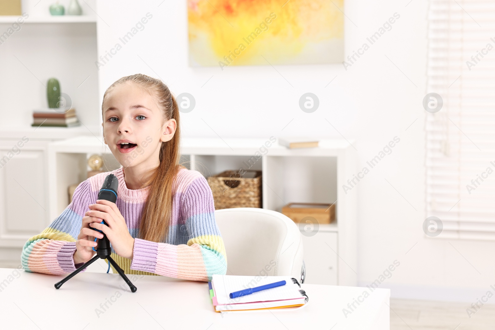 Photo of Little girl with microphone at white table indoors, space for text