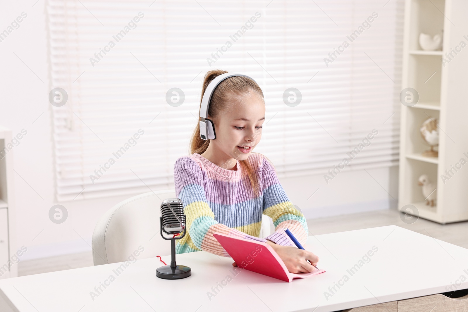 Photo of Little girl with microphone and headphones at white table indoors