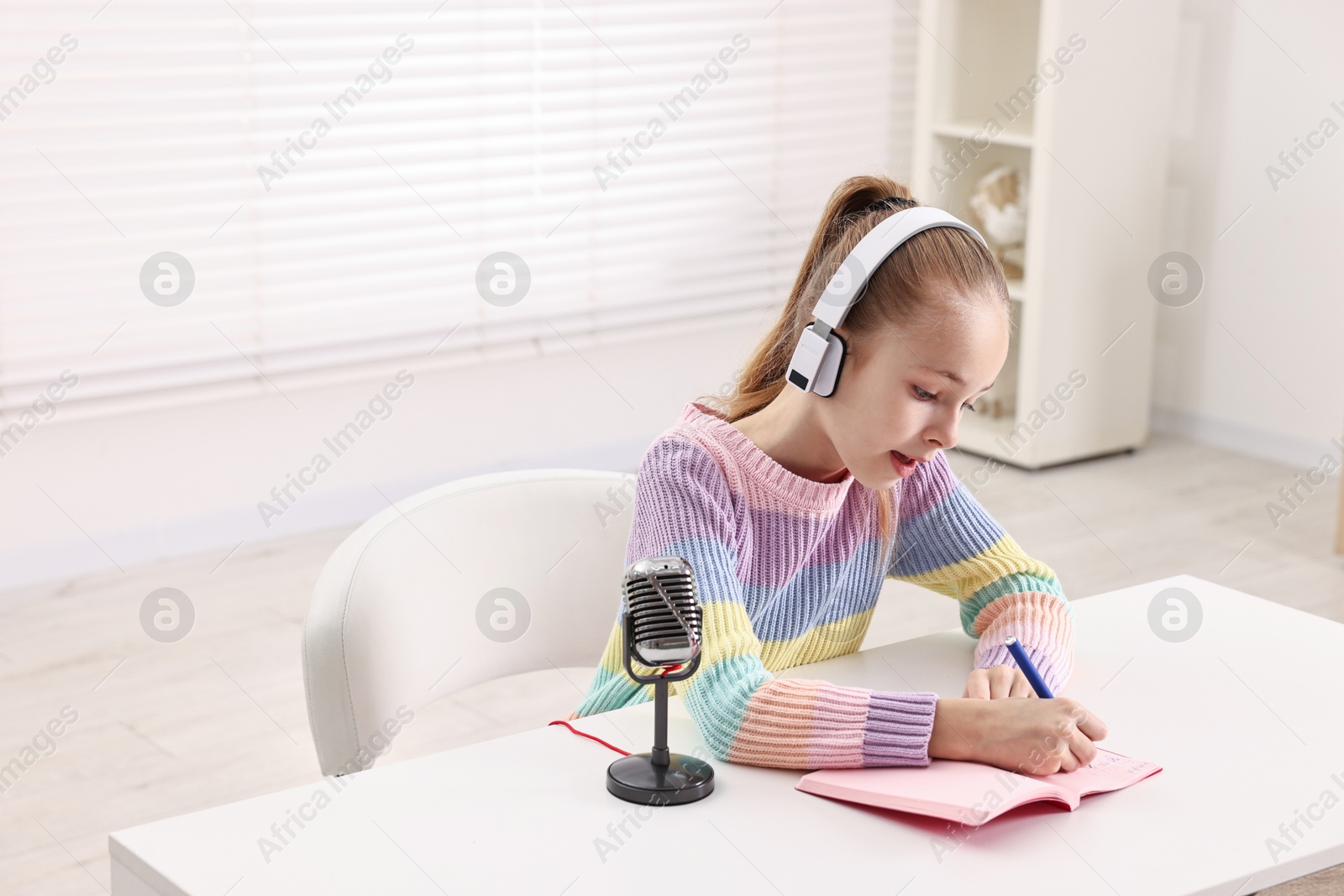 Photo of Little girl with microphone and headphones at white table indoors, space for text