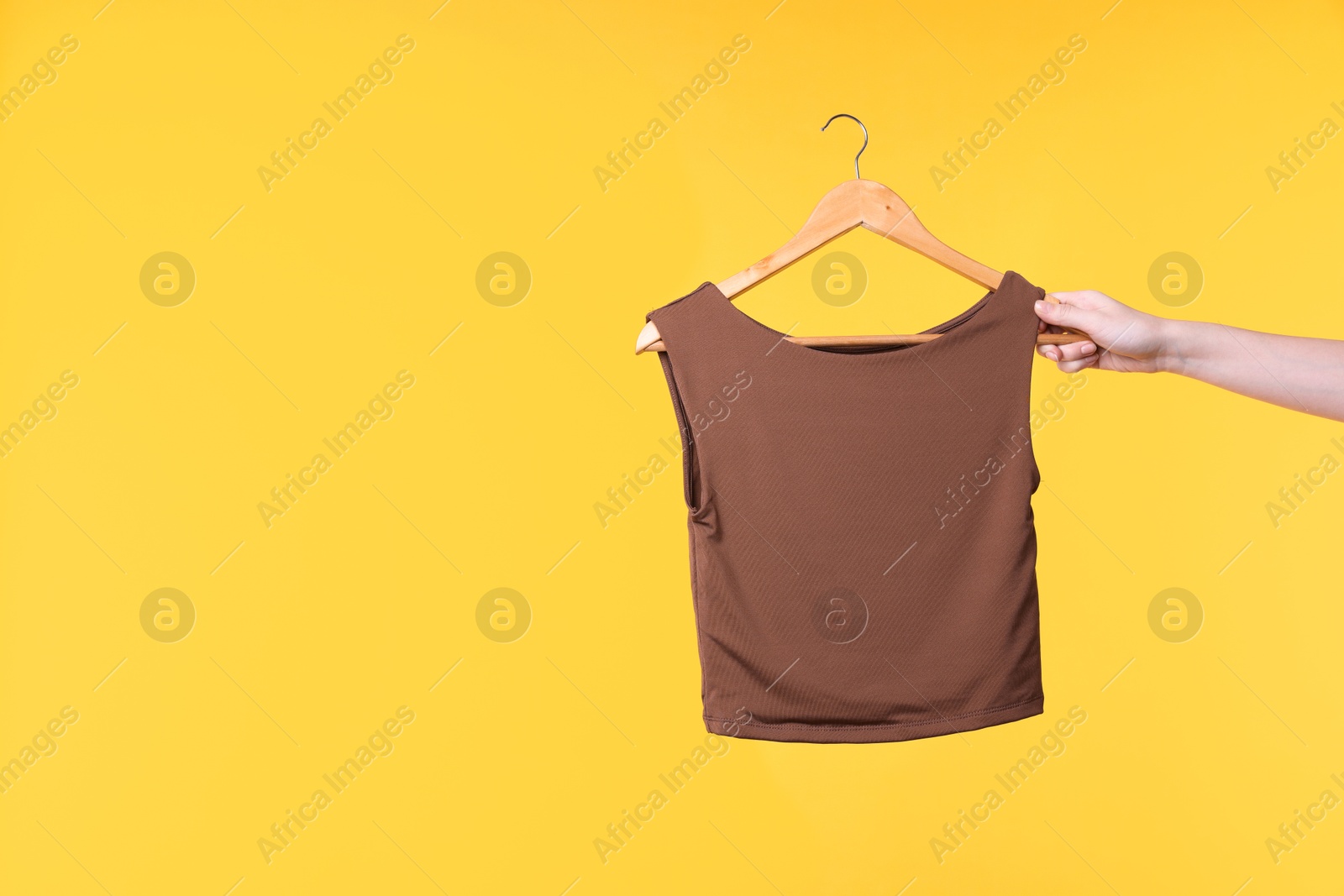 Photo of Woman holding hanger with brown tank top on yellow background, closeup. Space for text