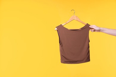 Photo of Woman holding hanger with brown tank top on yellow background, closeup. Space for text