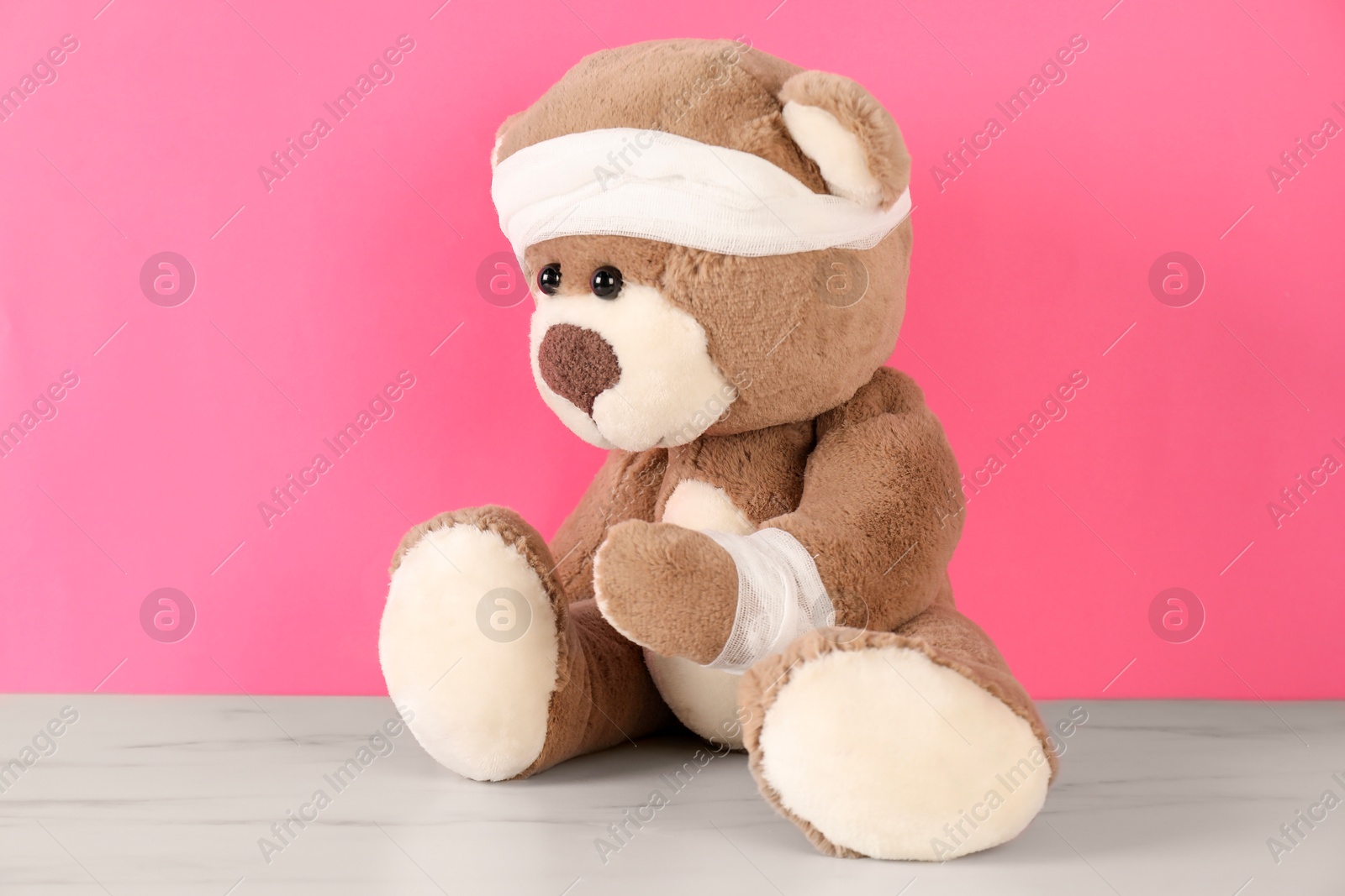 Photo of Teddy bear with bandages on white marble table against pink background