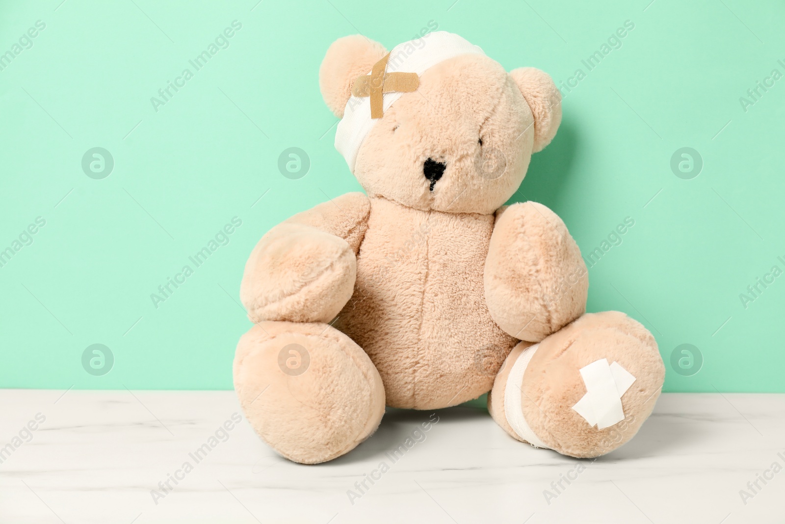 Photo of Teddy bear with bandages and sticking plasters on white marble table against turquoise background