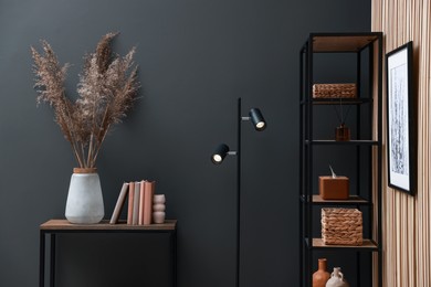 Photo of Console table with decor, shelving unit and lamp near grey wall in room. Interior design