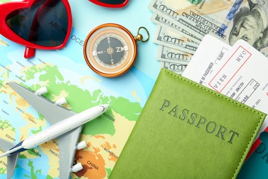 Photo of Passport with tickets, map, compass, plane model, money and sunglasses on light blue background, flat lay