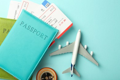 Photo of Passport with tickets, compass and plane model on light blue background, top view