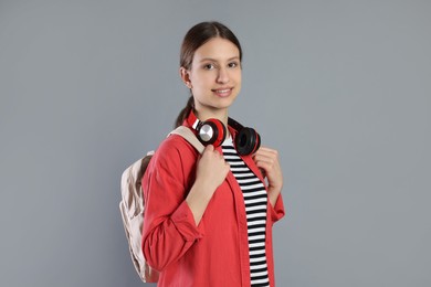 Photo of Portrait of smiling teenage girl with backpack and headphones on grey background