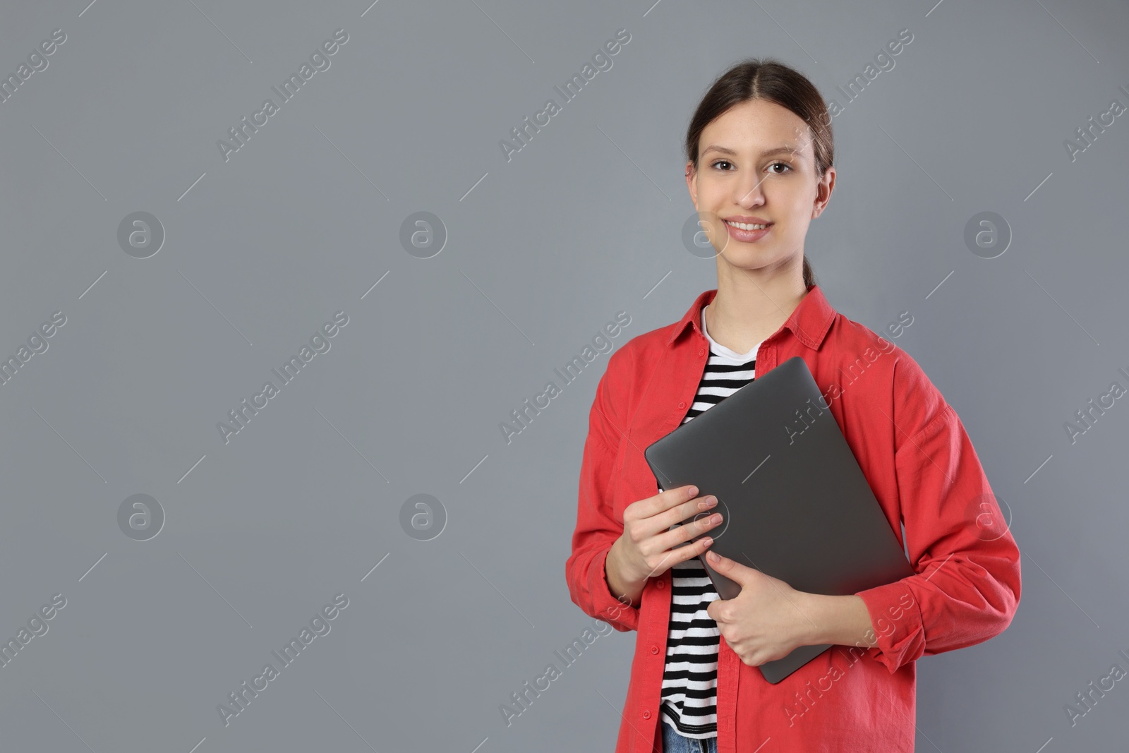 Photo of Portrait of smiling teenage girl with laptop on grey background. Space for text