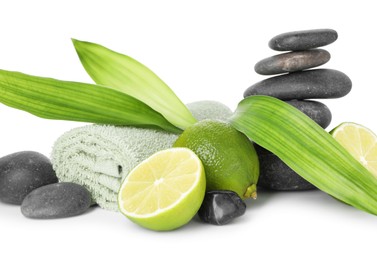Photo of Spa composition with limes, towel, massage stones and green leaves isolated on white
