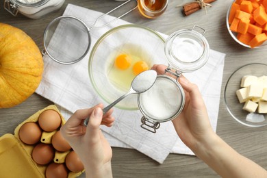 Photo of Making pumpkin pancakes. Woman adding sugar to eggs at wooden table, top view