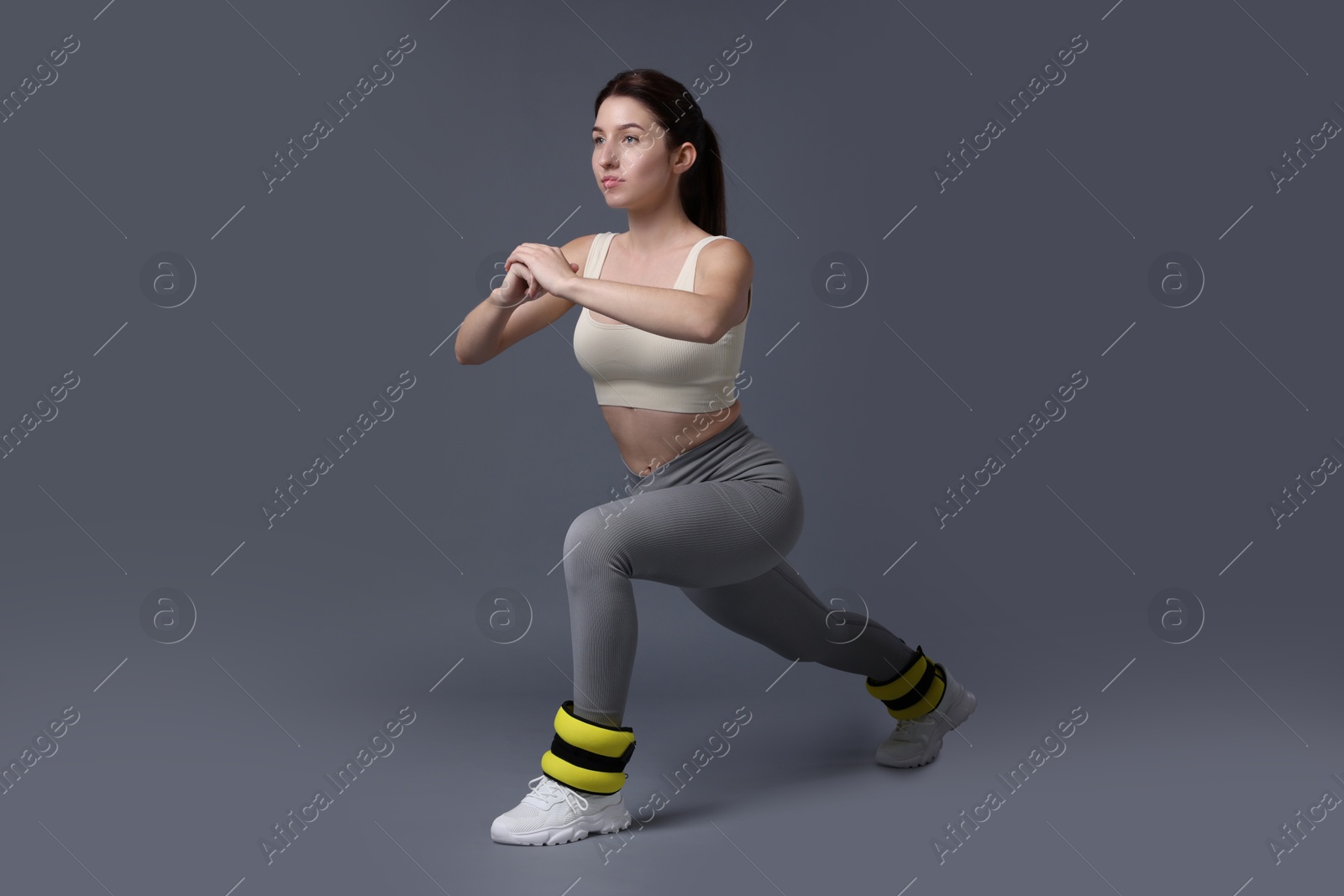 Photo of Woman in sportswear exercising with ankle weights on grey background