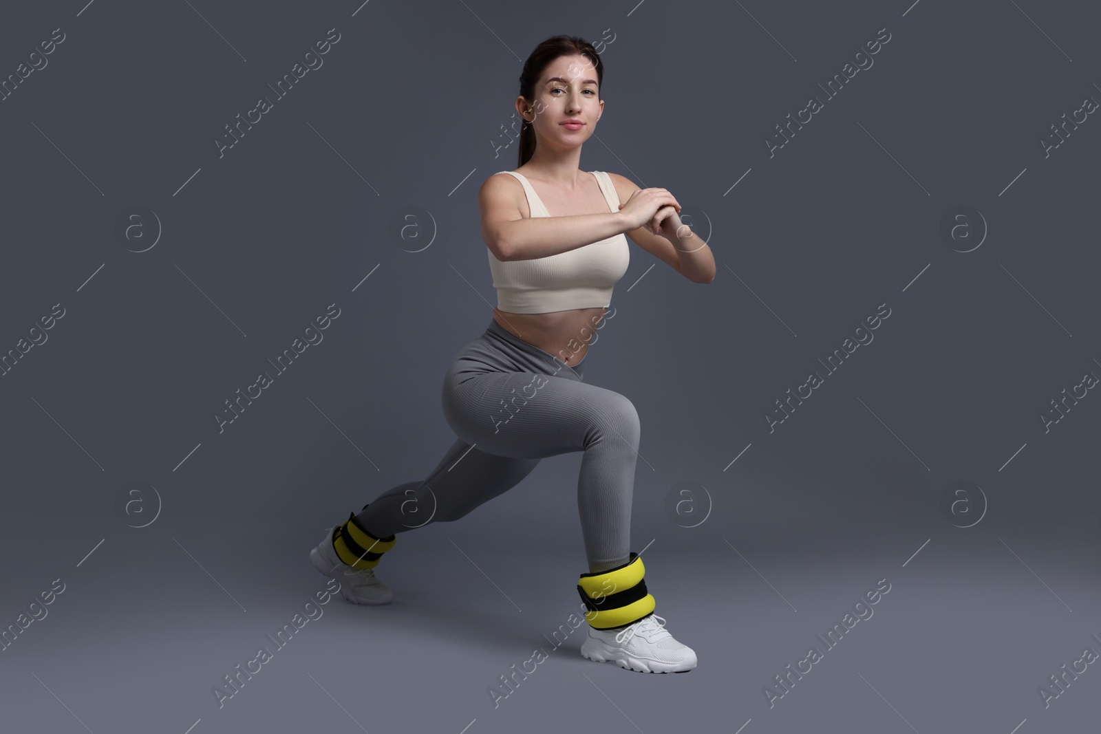 Photo of Woman in sportswear exercising with ankle weights on grey background