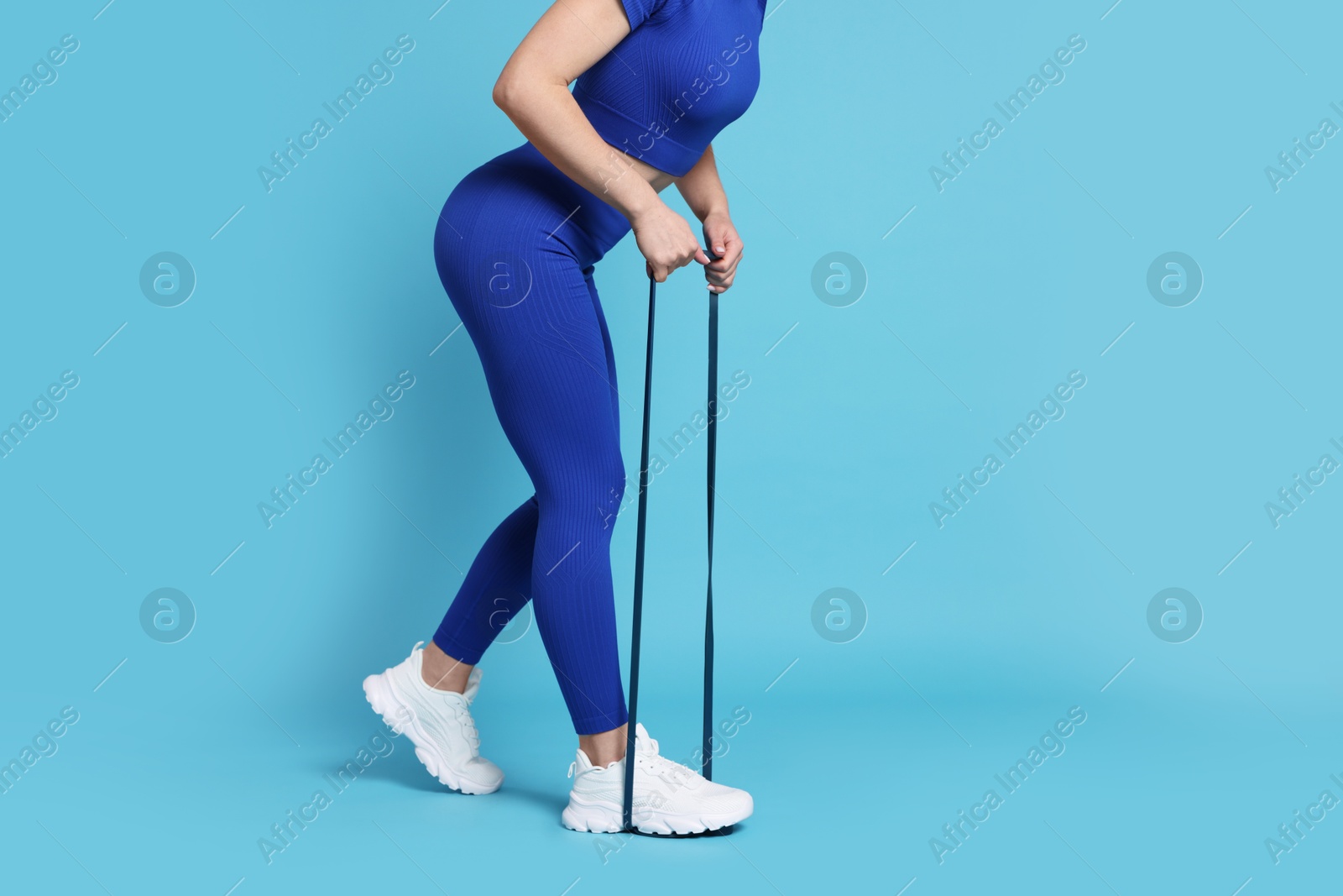 Photo of Woman in sportswear exercising elastic band on light blue background, closeup